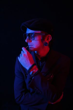 Portrait in dark room lit with red and blue neon lights featuring person in cap and sunglasses.