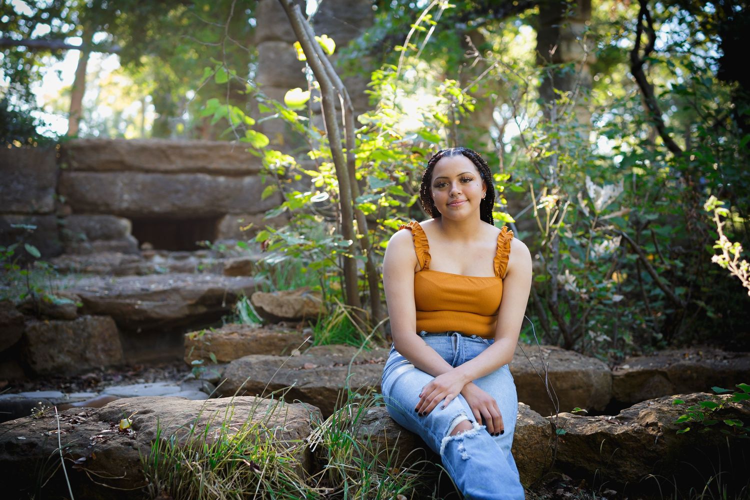 Person in yellow top sits on stone steps surrounded by lush garden foliage.