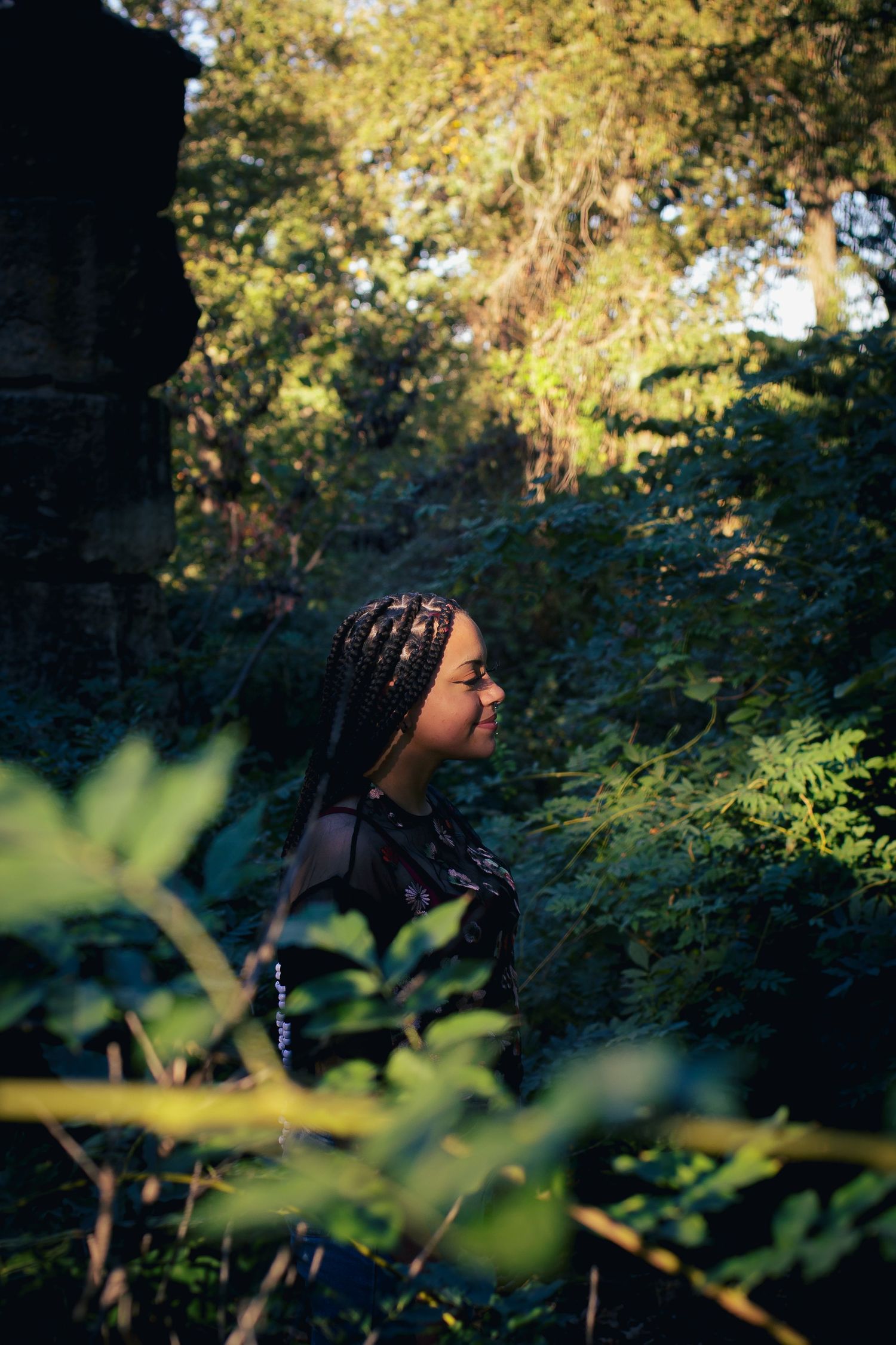 Profile view of person with braided hair among green foliage in natural setting.