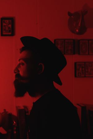 Side profile silhouette in red lighting wearing hat with wall decorations in background.