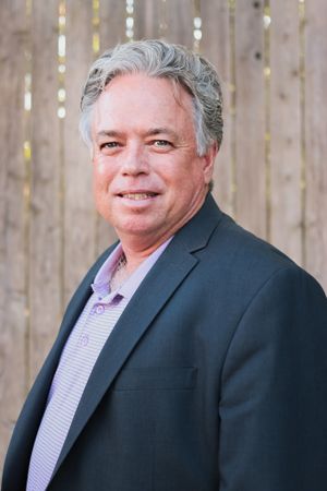 Professional portrait of person in business suit against wooden fence backdrop.