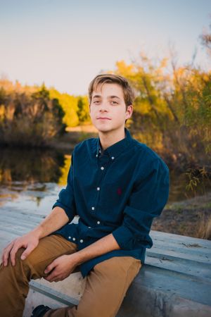 Portrait by lake during golden hour with autumn foliage in background.