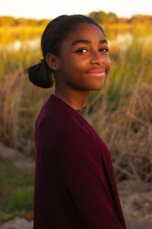 Portrait of someone in a burgundy sweater against a golden sunset field background.