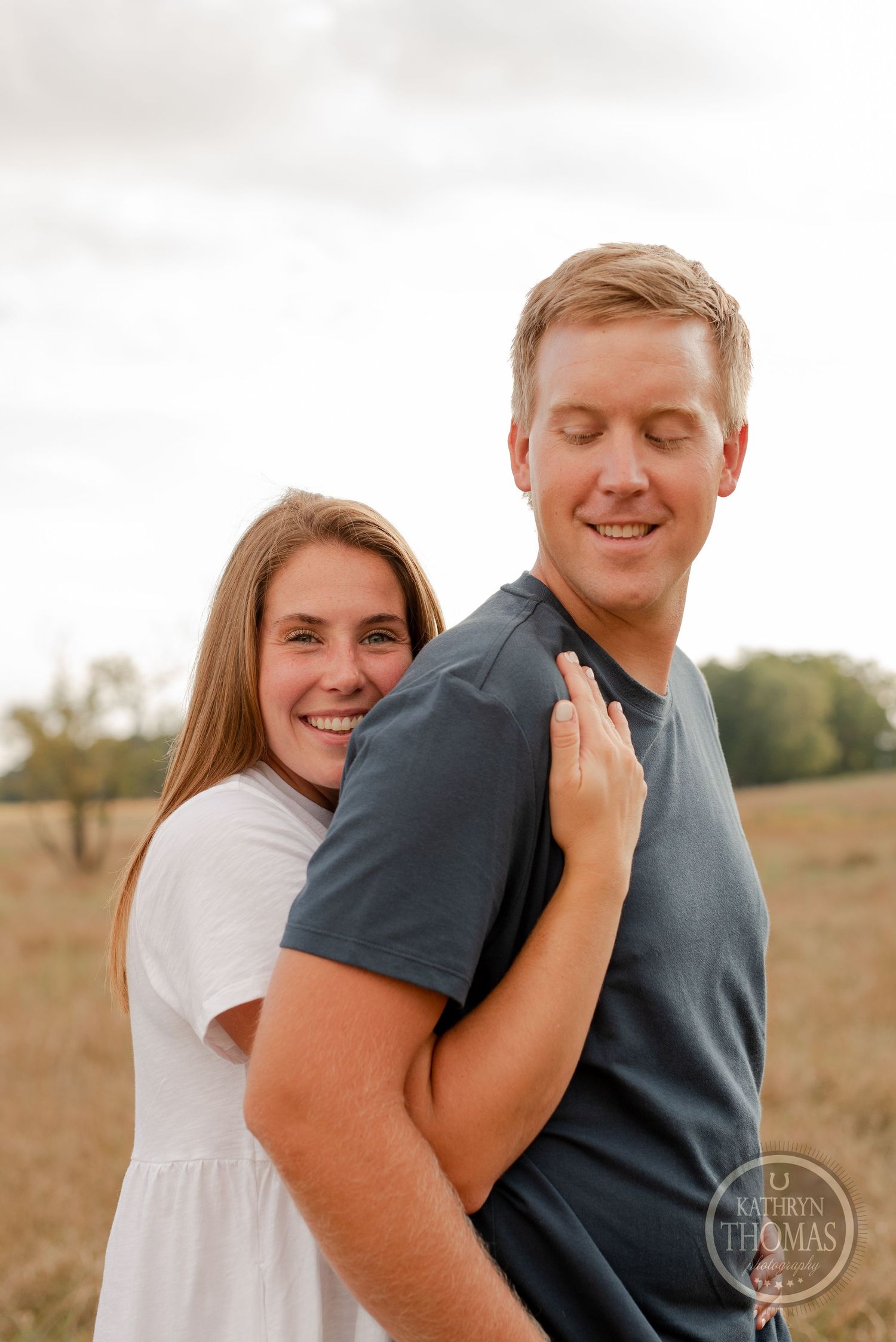 Happy couple embracing outdoors in casual attire against a natural landscape.