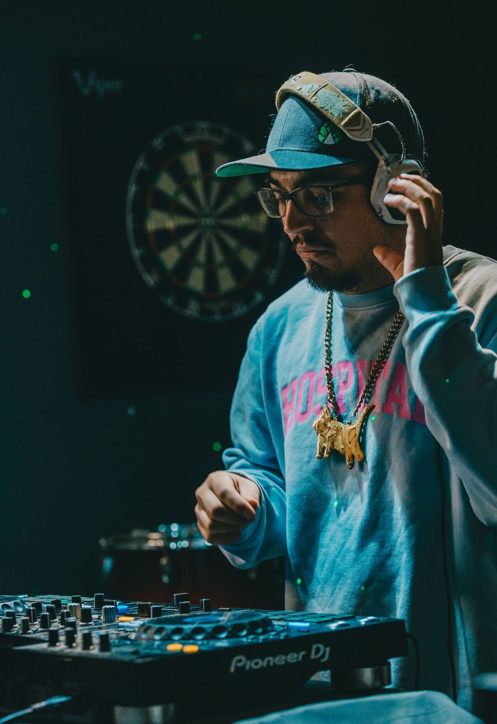 DJ mixing music on Pioneer equipment while wearing blue cap and headphones.