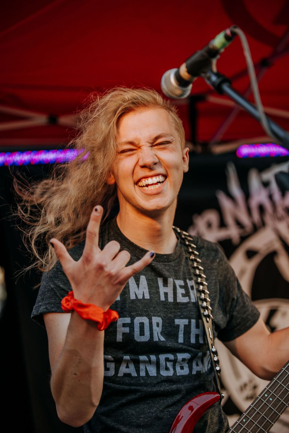 An energetic band member with blonde hair makes rock gesture while performing on stage.