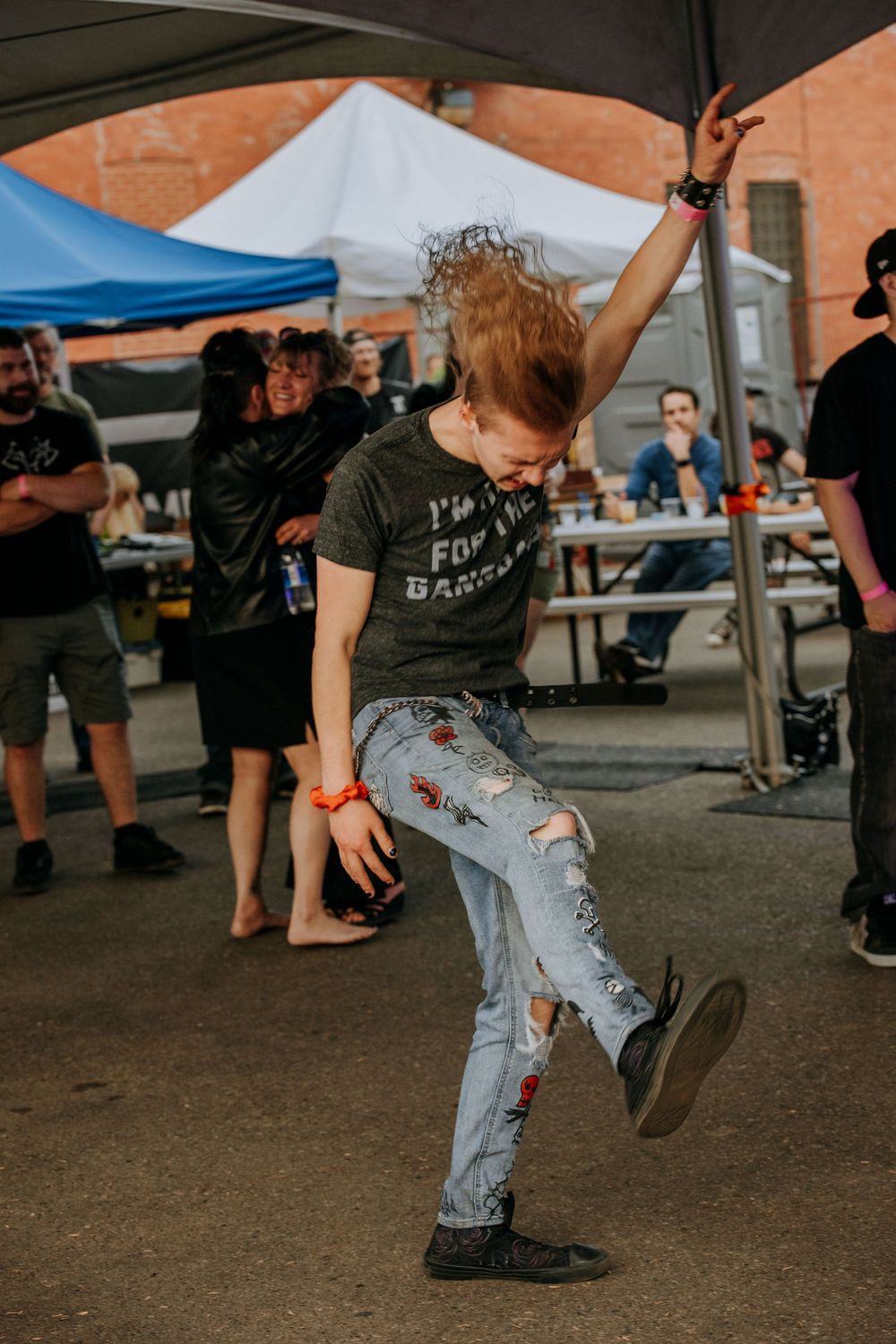 A performer in ripped jeans kicks energetically during an outdoor music festival.