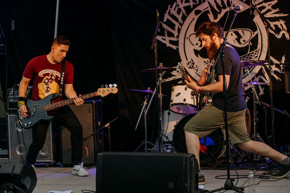 Musicians performing on stage with guitar and microphone during outdoor show.
