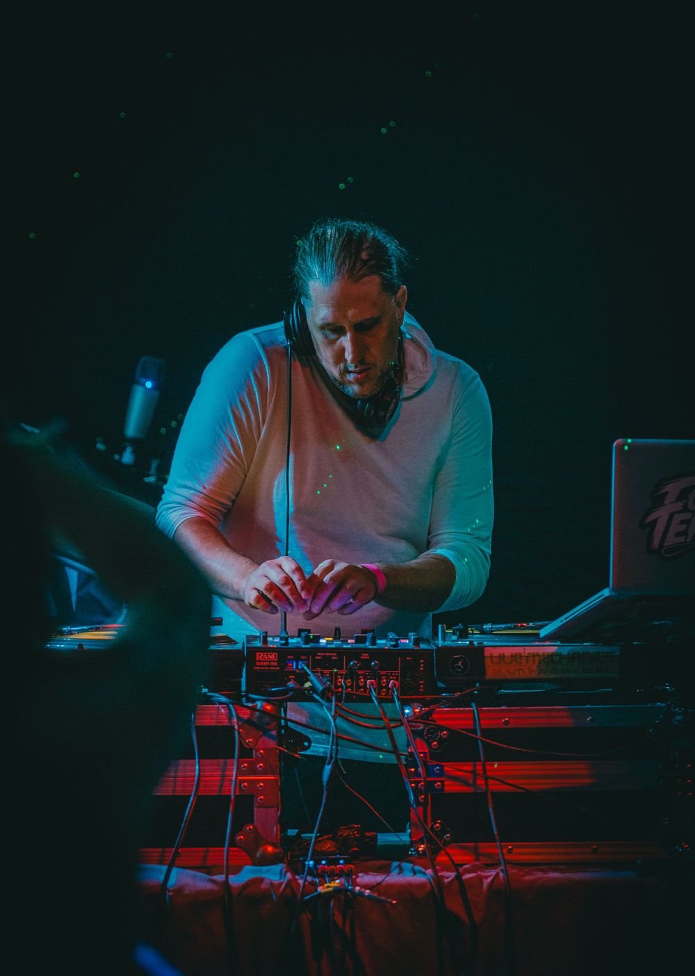 DJ performing with electronic music equipment under blue and red stage lighting.