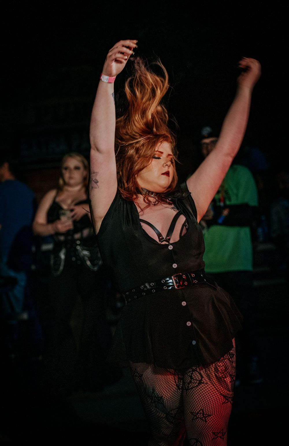Concert goer dancing with arms raised in black dress at dark music venue.