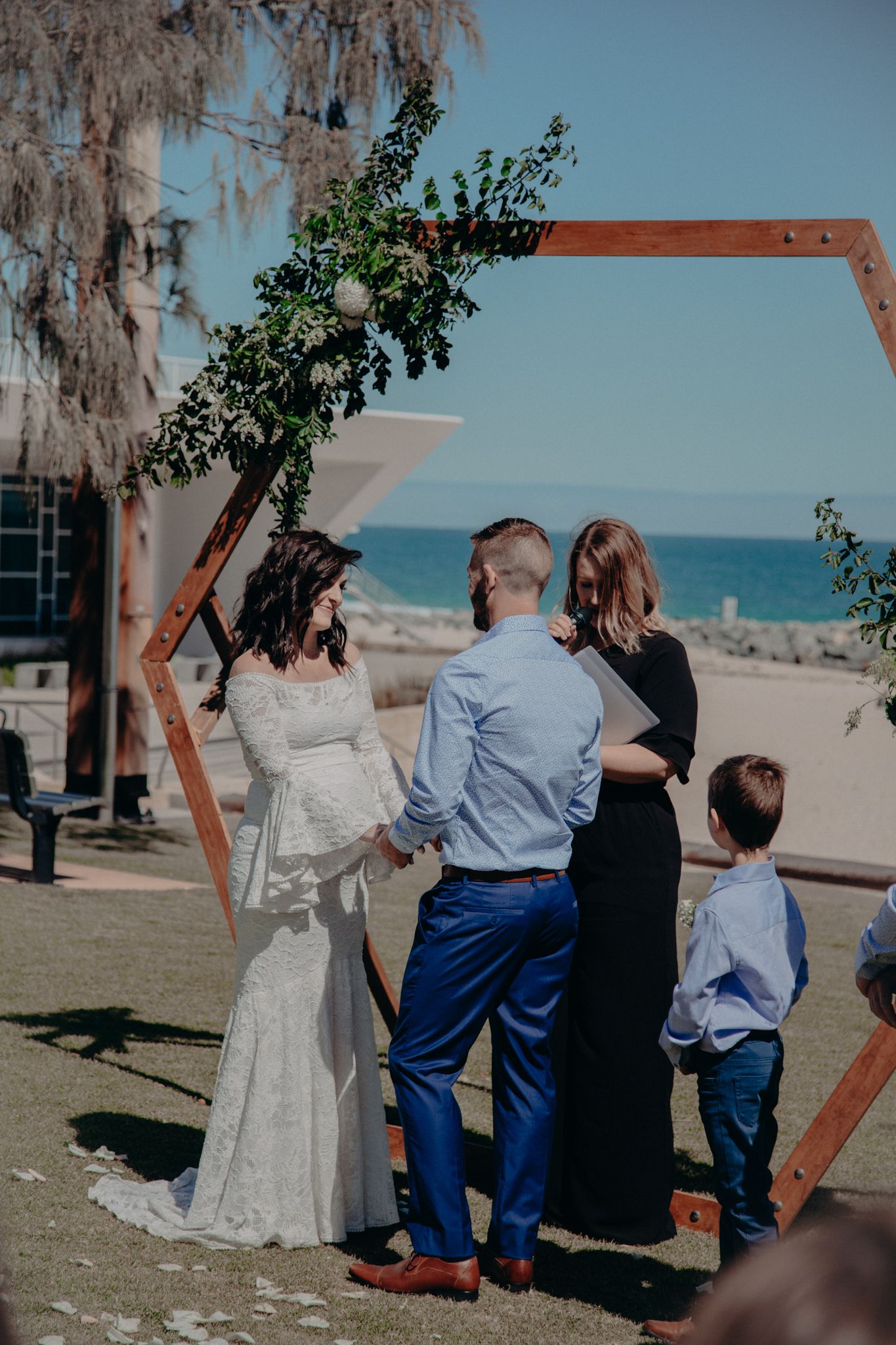 A wedding ceremony taking place under a wooden arch frame with ocean views.