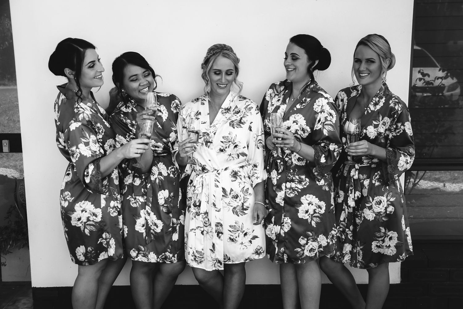 Five women in matching floral robes pose together for a black and white wedding photo.