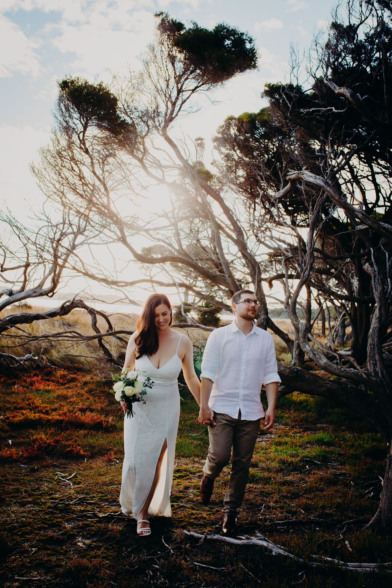 A couple poses together in front of windswept trees during a romantic outdoor photoshoot.