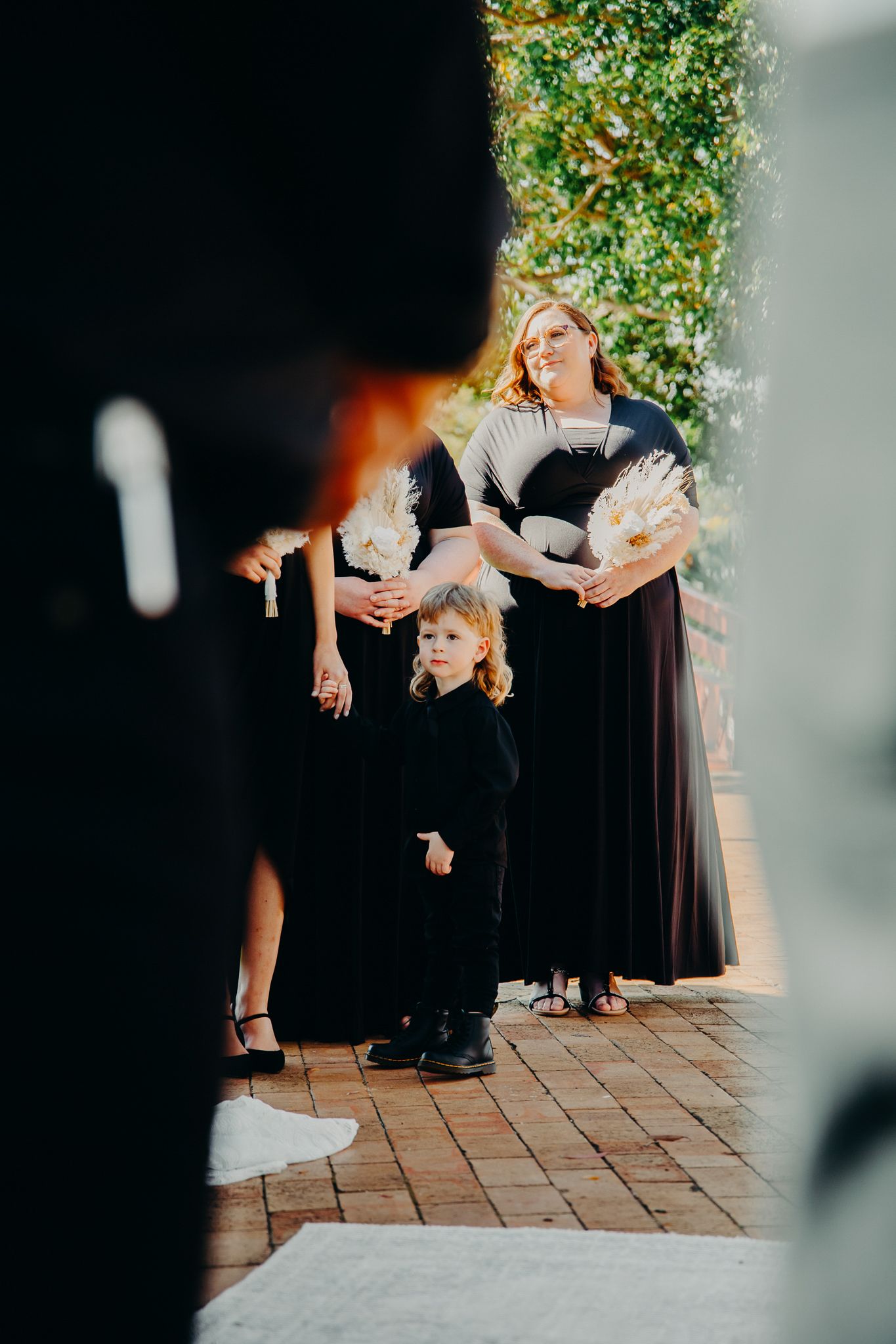 A candid moment during a wedding ceremony with guests in formal attire on a brick patio.