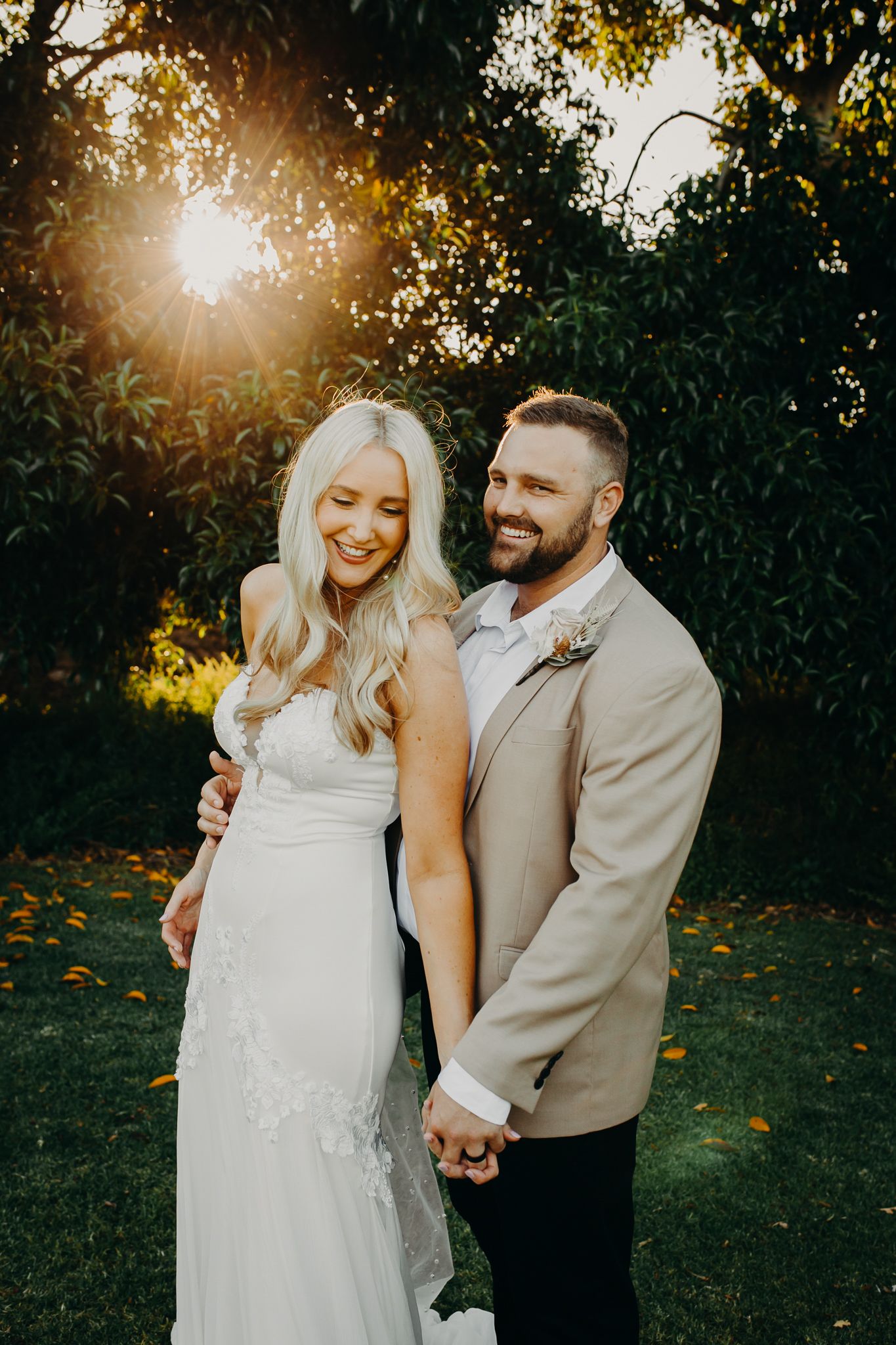 A romantic wedding couple shares a candid moment at sunset in a garden setting.