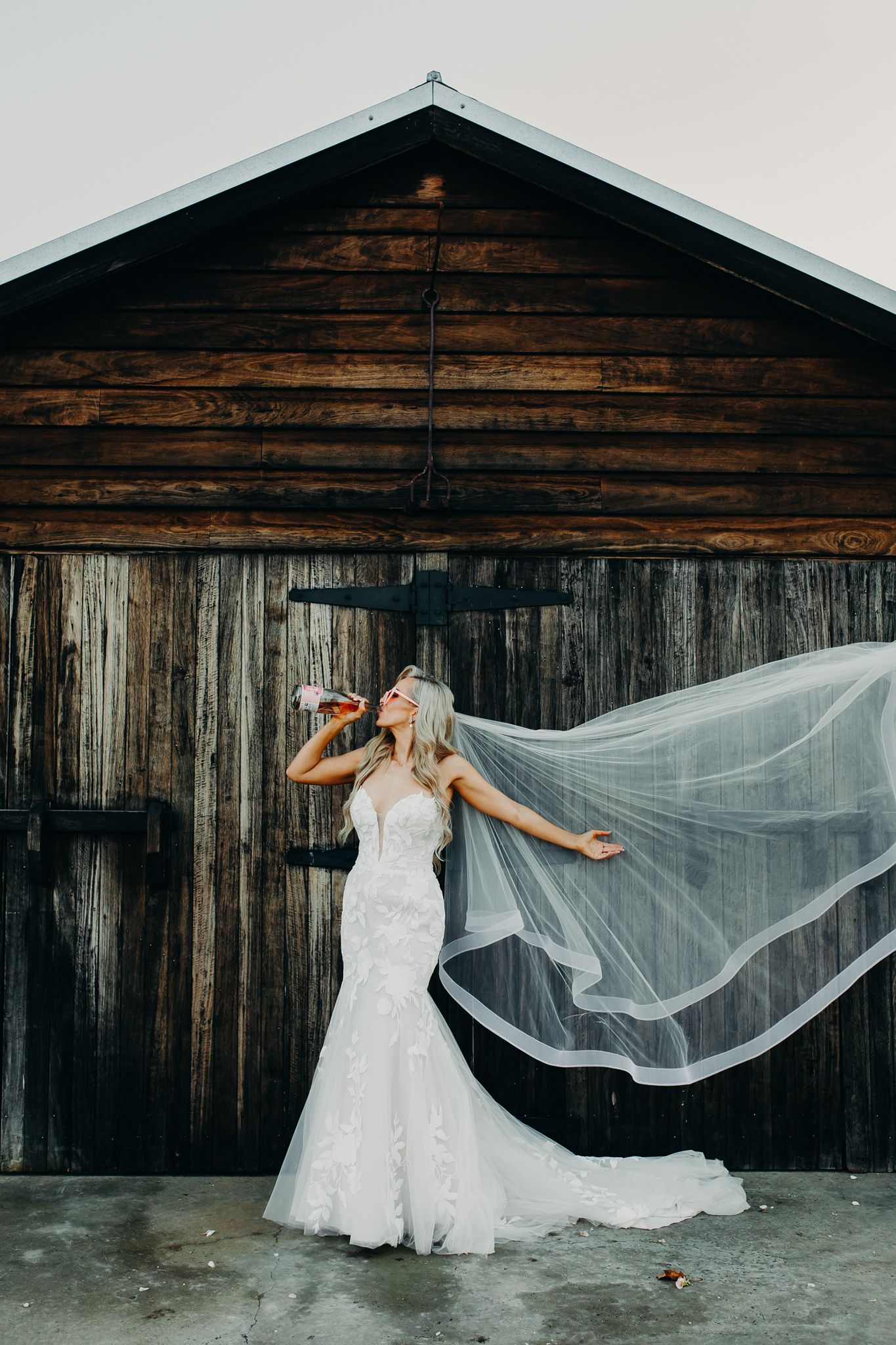 White wedding dress and flowing veil dramatically photographed against rustic wooden barn.