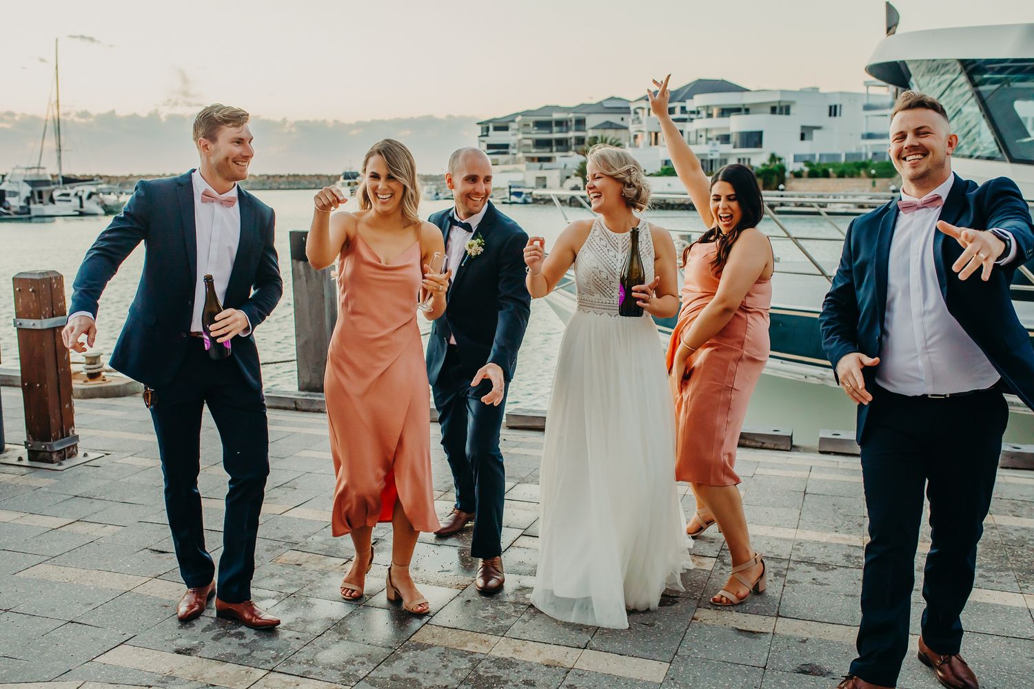 Wedding party celebrates on dock with champagne at waterfront venue.