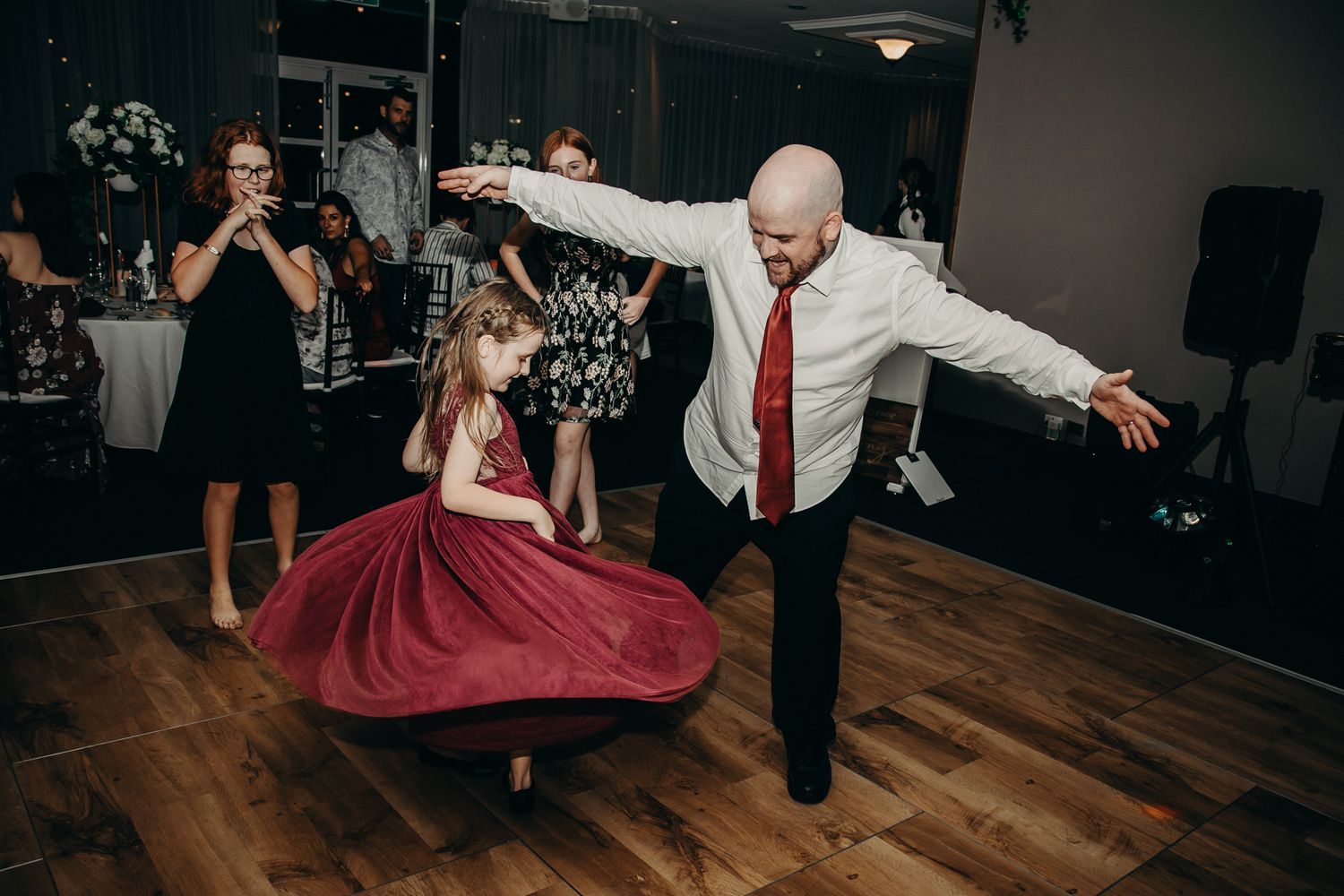 Dynamic dance floor moment captured during wedding reception on wooden floor.