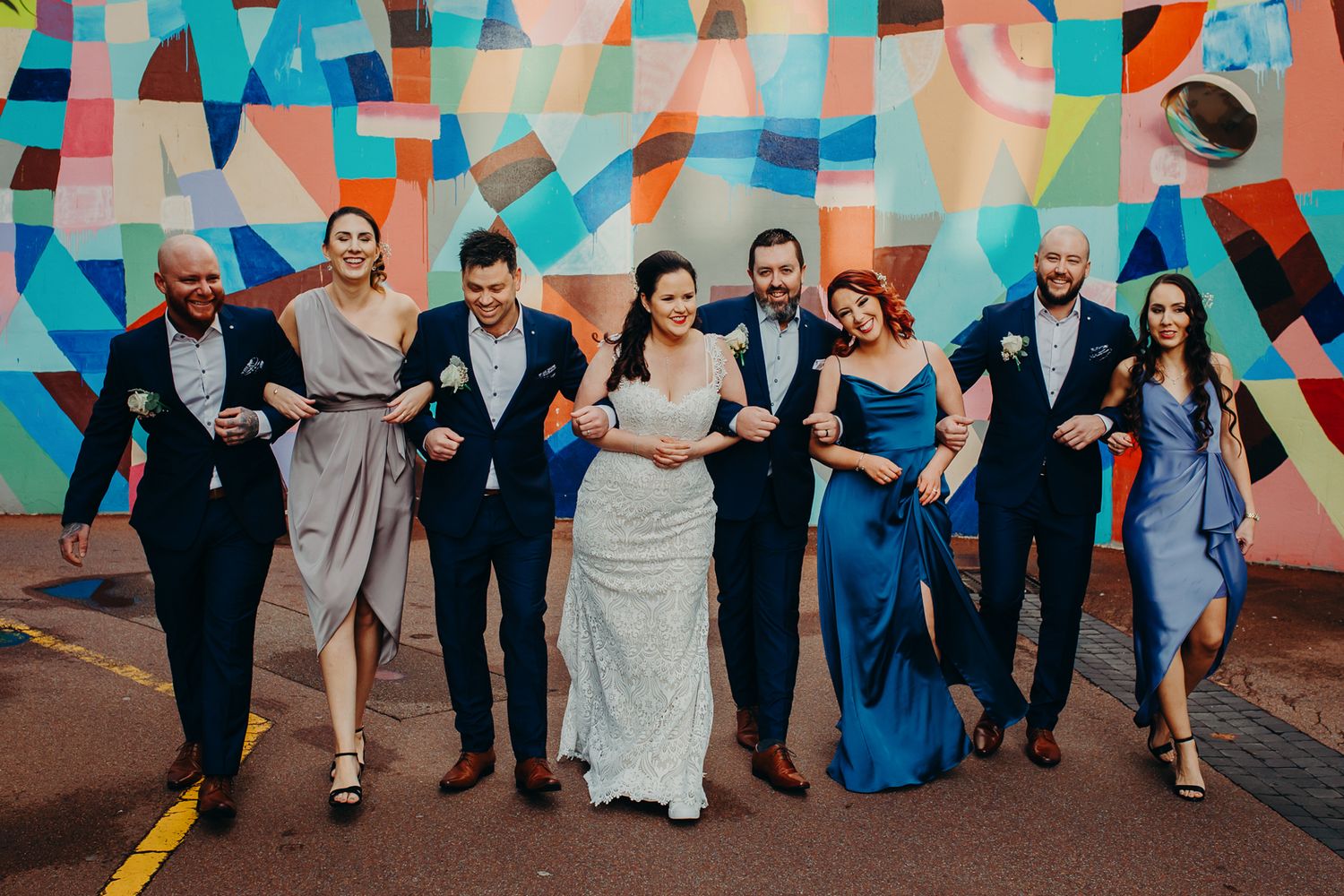 Wedding party poses together against colorful geometric wall mural.