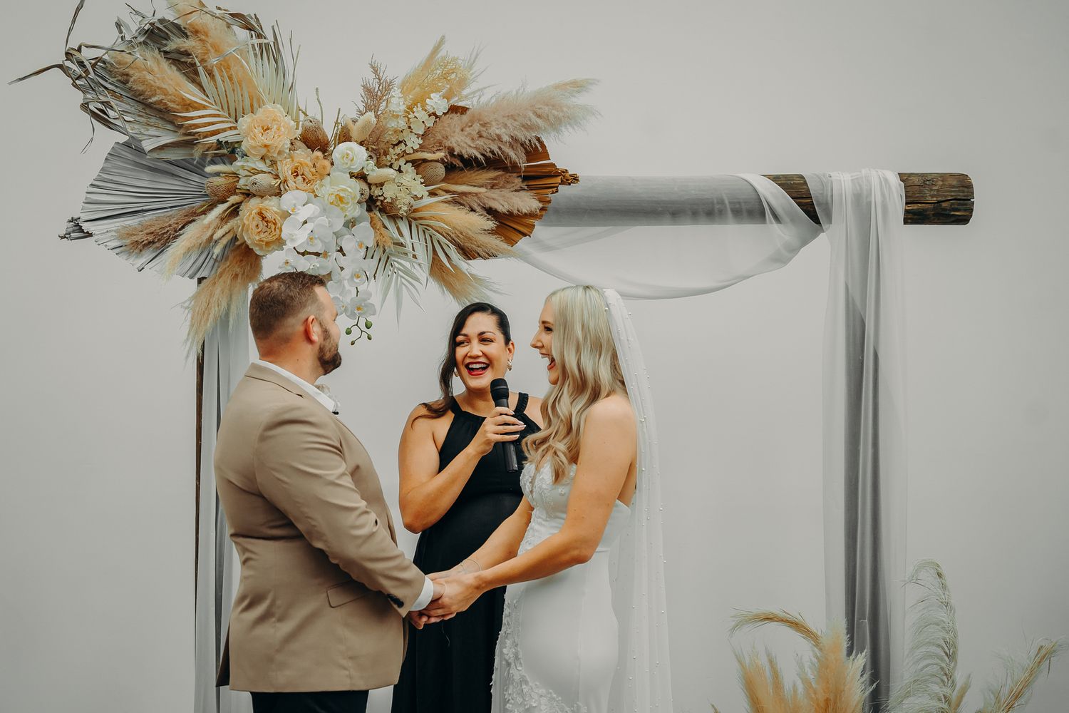 Wedding ceremony under arch with dried floral arrangements and neutral tones.
