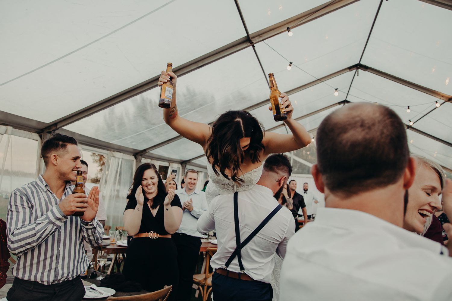 Wedding guests celebrate joyfully in a white tent during reception festivities.
