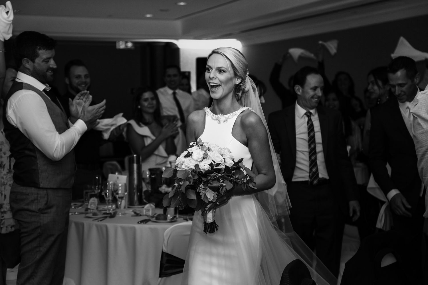 A bride in white dress holds bouquet while dancing at indoor reception.