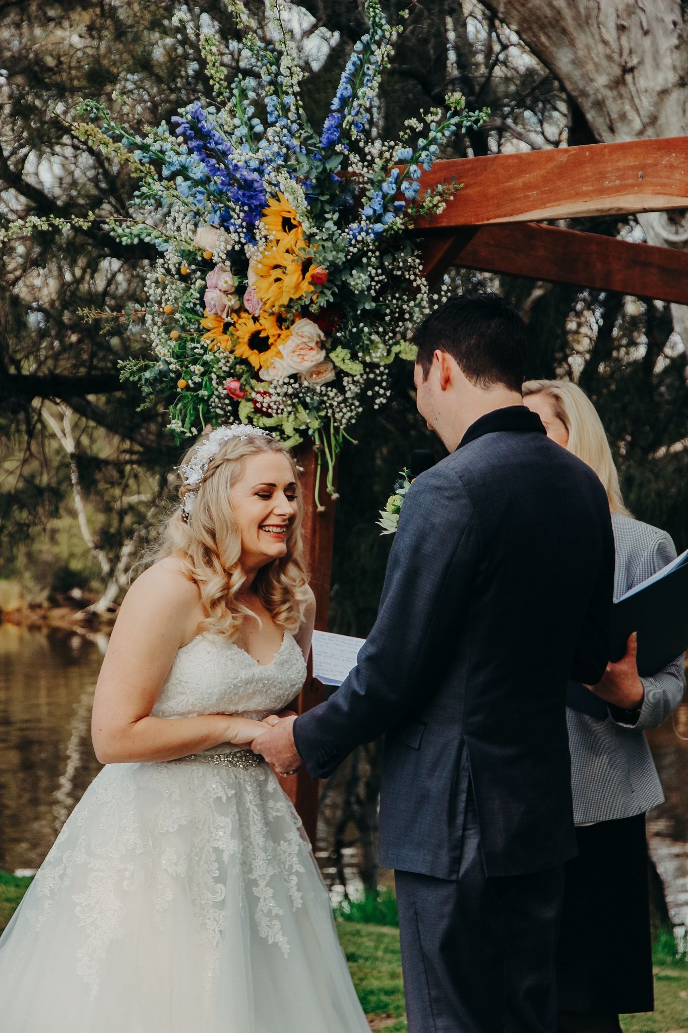 A wedding ceremony outdoors with sunflowers and blue flowers in rustic arch decoration.