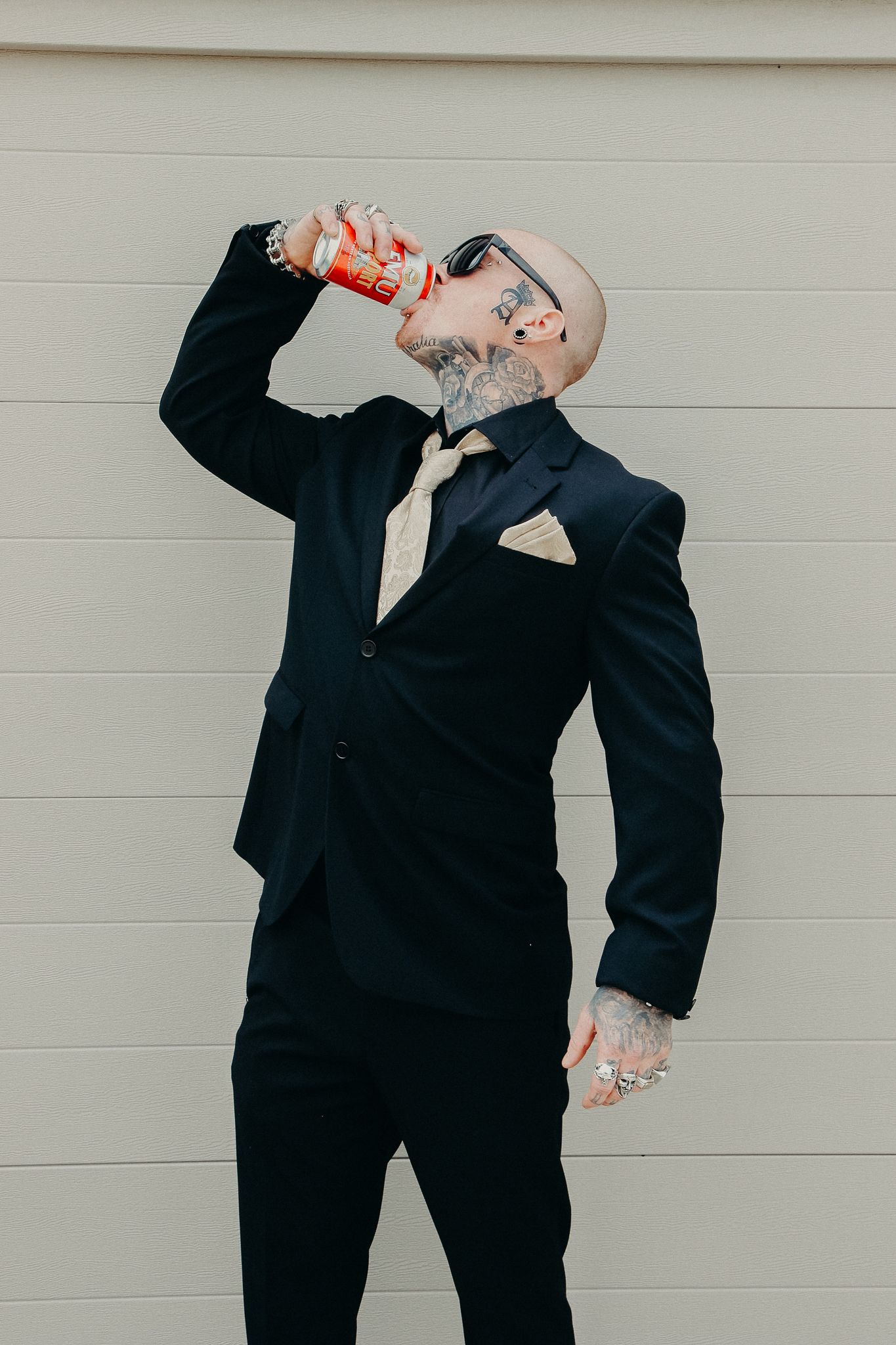 Person in dark suit drinks from bottle against white wall background.
