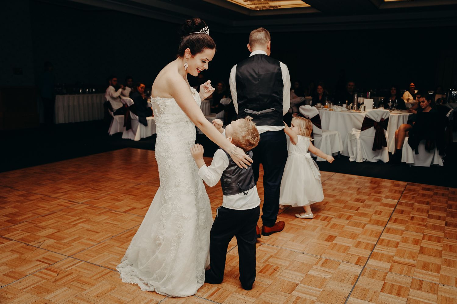 Wedding reception scene showing dancing on a wooden floor in a dimly lit ballroom.
