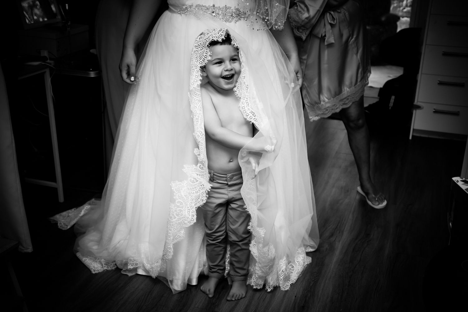 Black and white photo of small child standing beneath wedding dress.