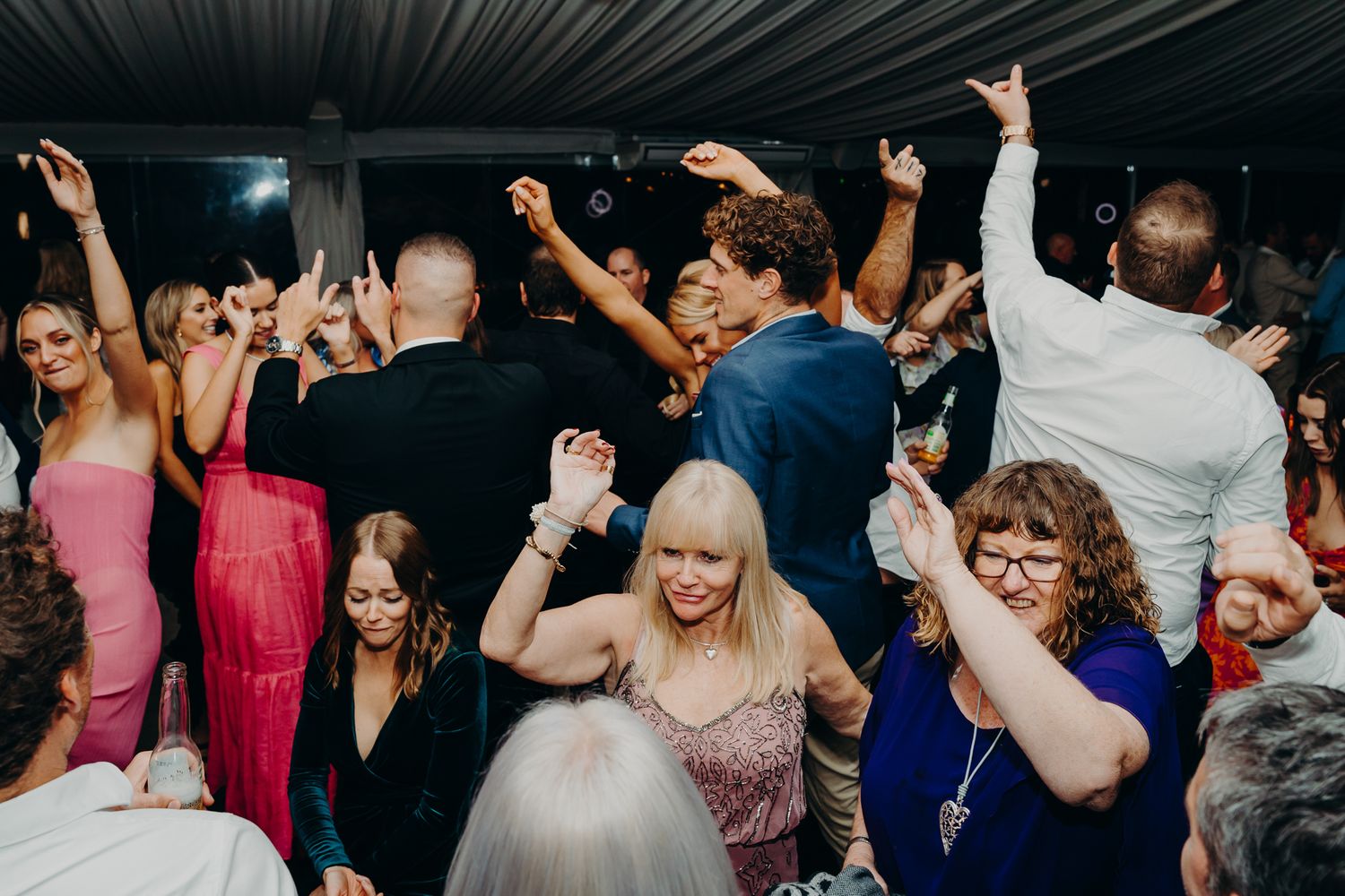 Festive crowd dances and celebrates under a tent at a wedding reception.