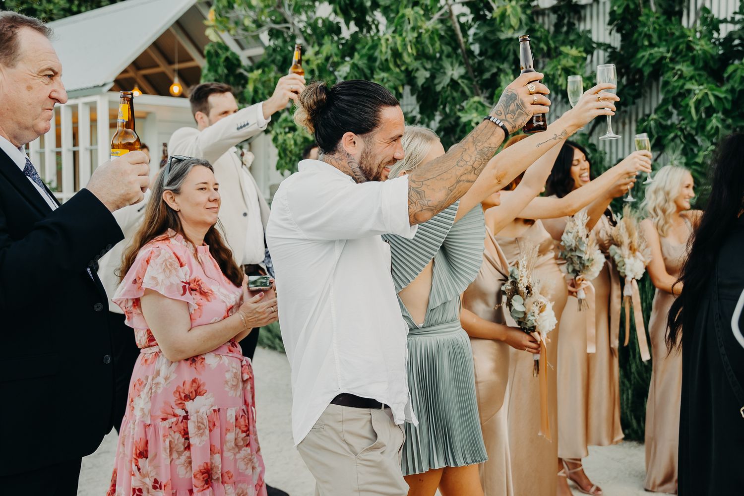Wedding guests raise their glasses for a toast during an outdoor celebration.
