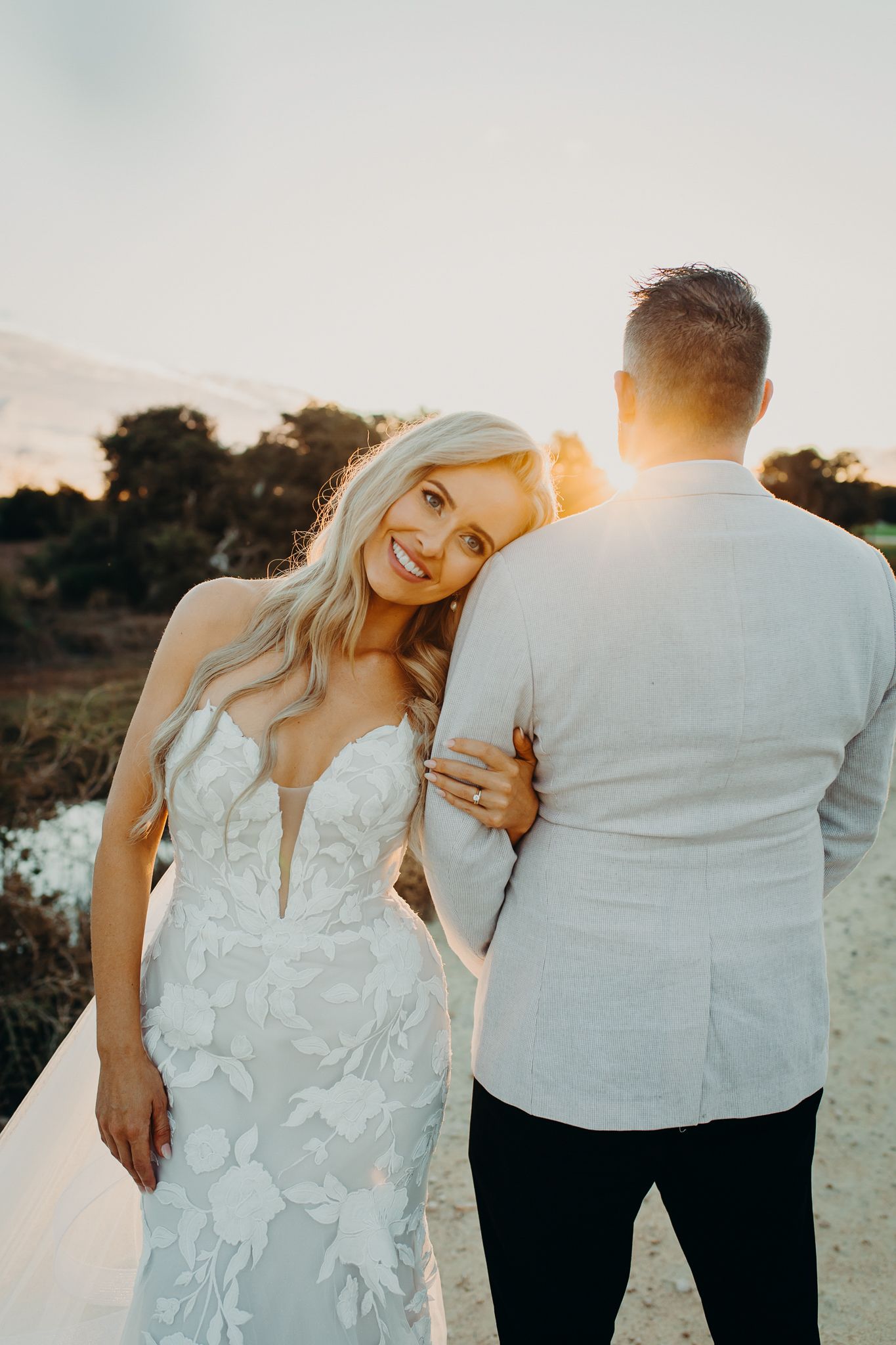 Couple in wedding attire poses together during golden hour sunset.