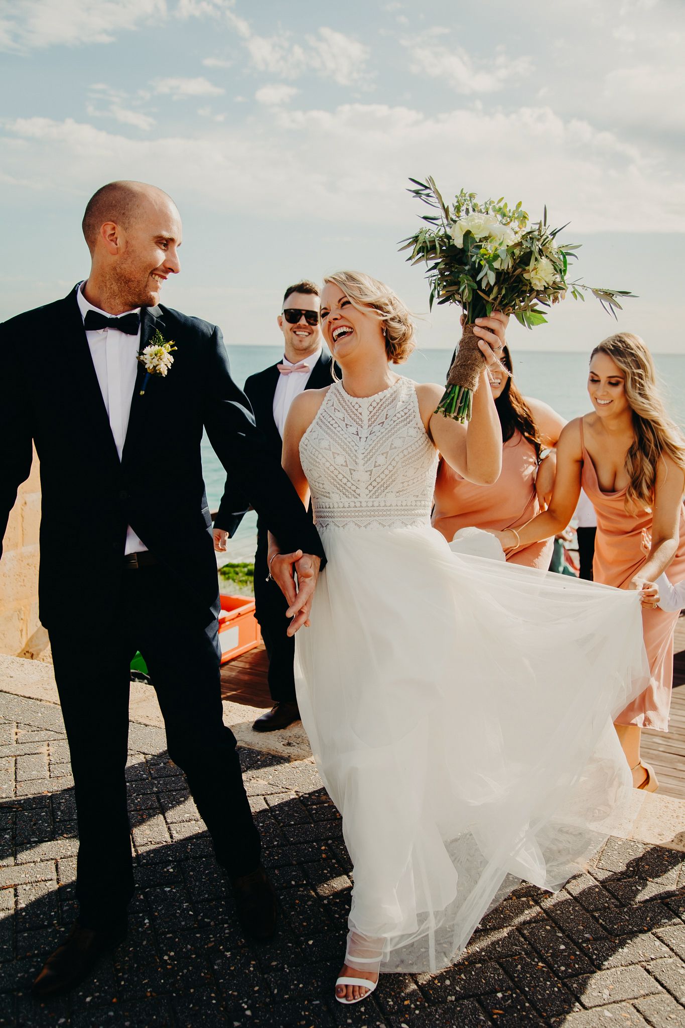 Wedding party celebrating on a sunny patio with bride holding a white and green bouquet.