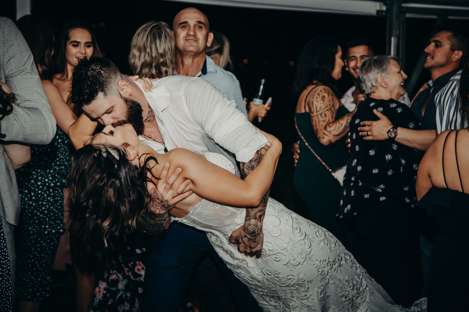 Joyful couple performs dramatic dance dip during wedding reception celebration.