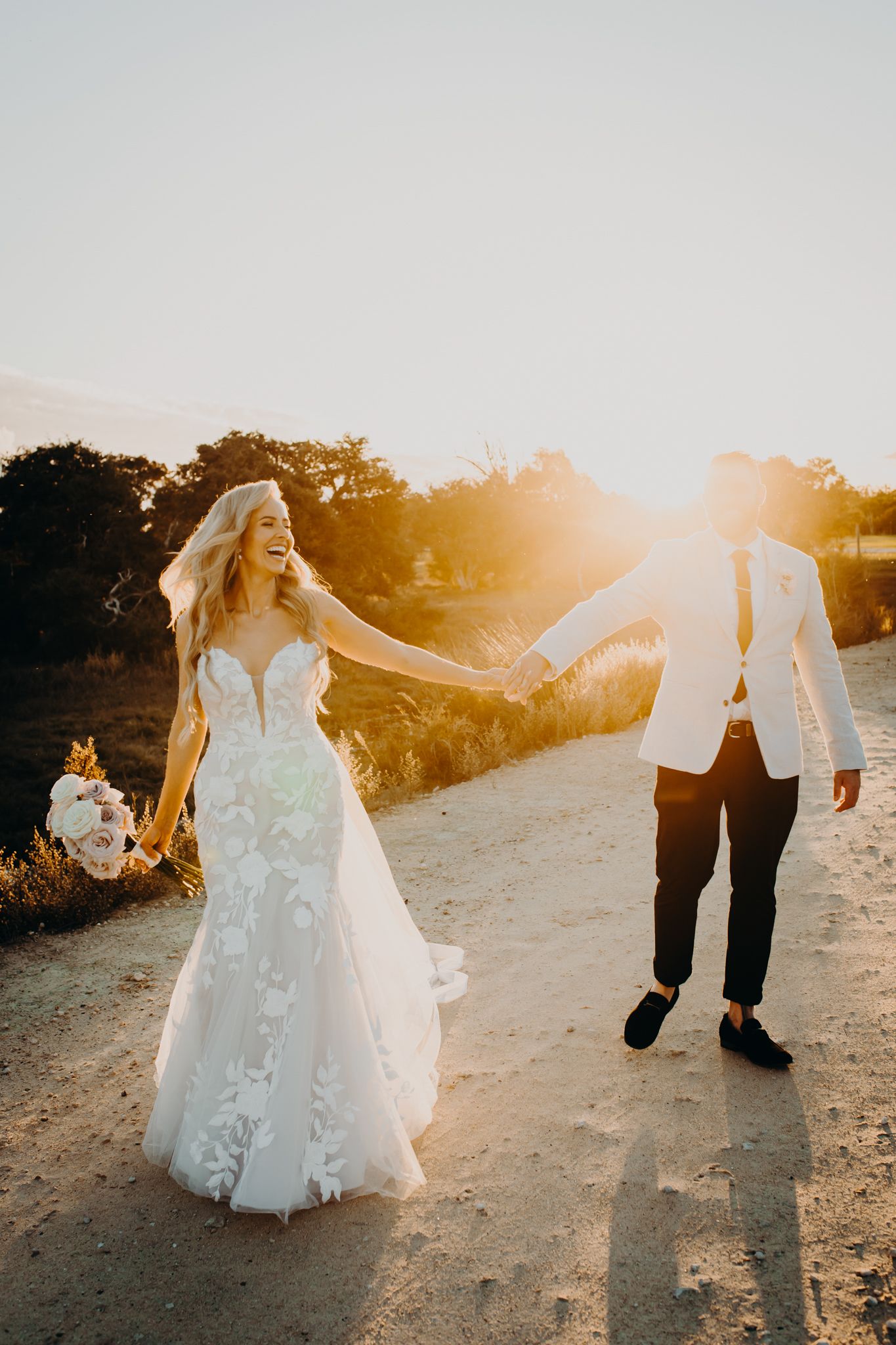 Romantic sunset wedding photo of couple walking on a dirt path with golden light.
