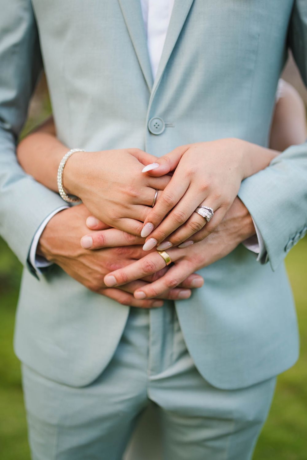 Close-up of hands wearing wedding rings with a light blue suit jacket in the background.