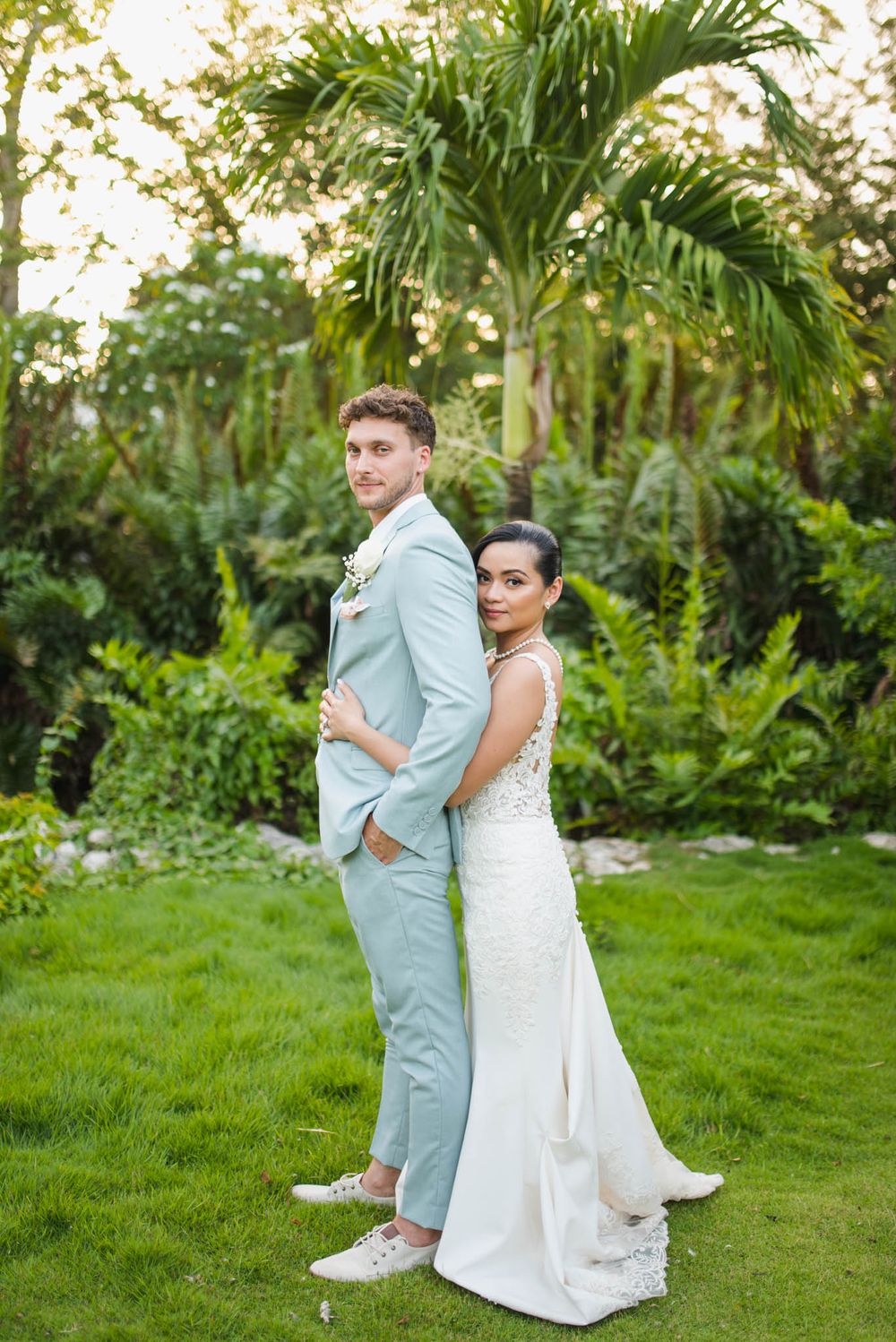 Newlyweds pose in a lush tropical garden setting with palm trees and greenery.