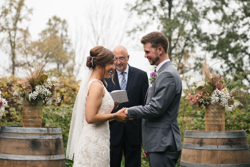 Outdoor wedding ceremony with couple exchanging vows in front of wine barrels and floral arrangements.