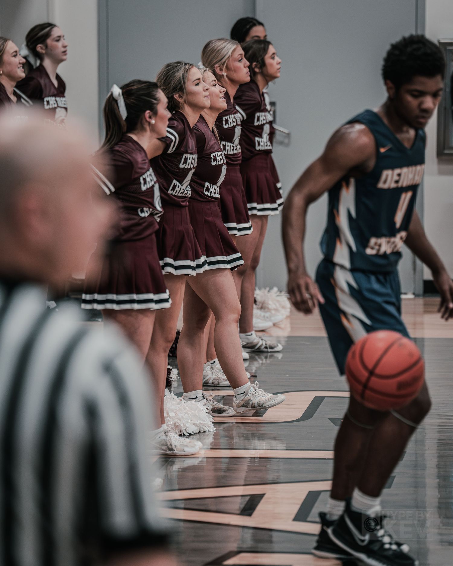 Cheerleaders in maroon uniforms line up courtside during a basketball game.