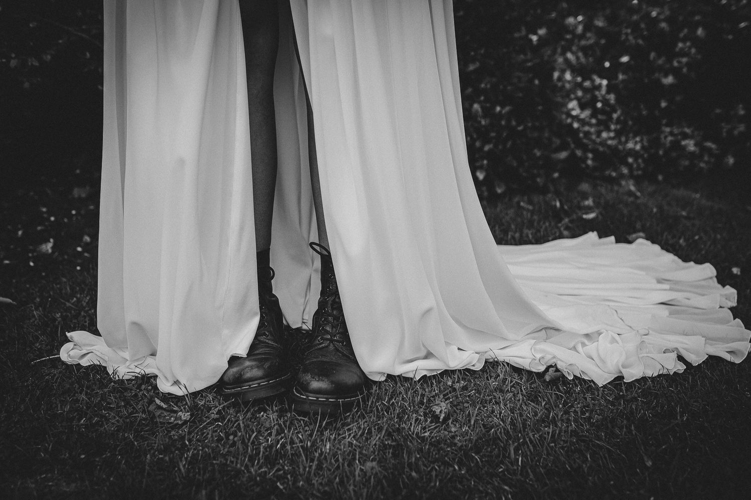Black and white photo of wedding dress trains trailing on outdoor ground.