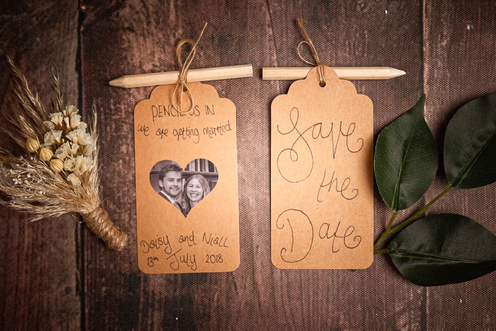 Two save-the-date tags with decorative details and dried flowers on wooden surface.