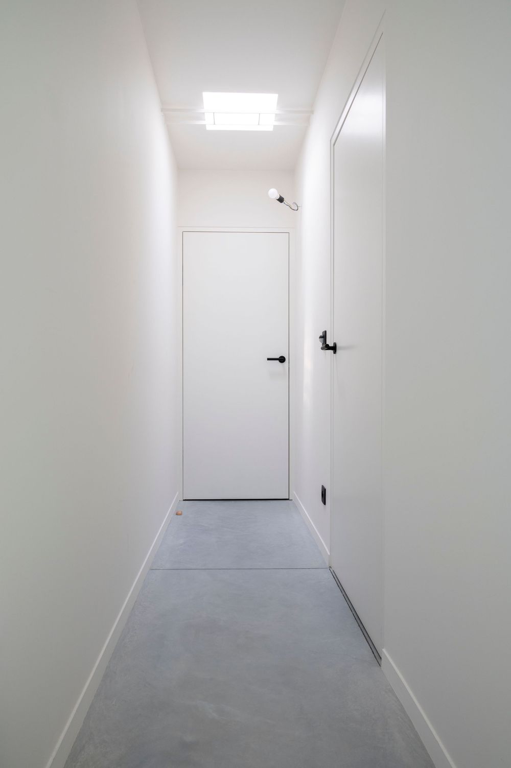 Long white hallway with concrete floor and minimalist doors.