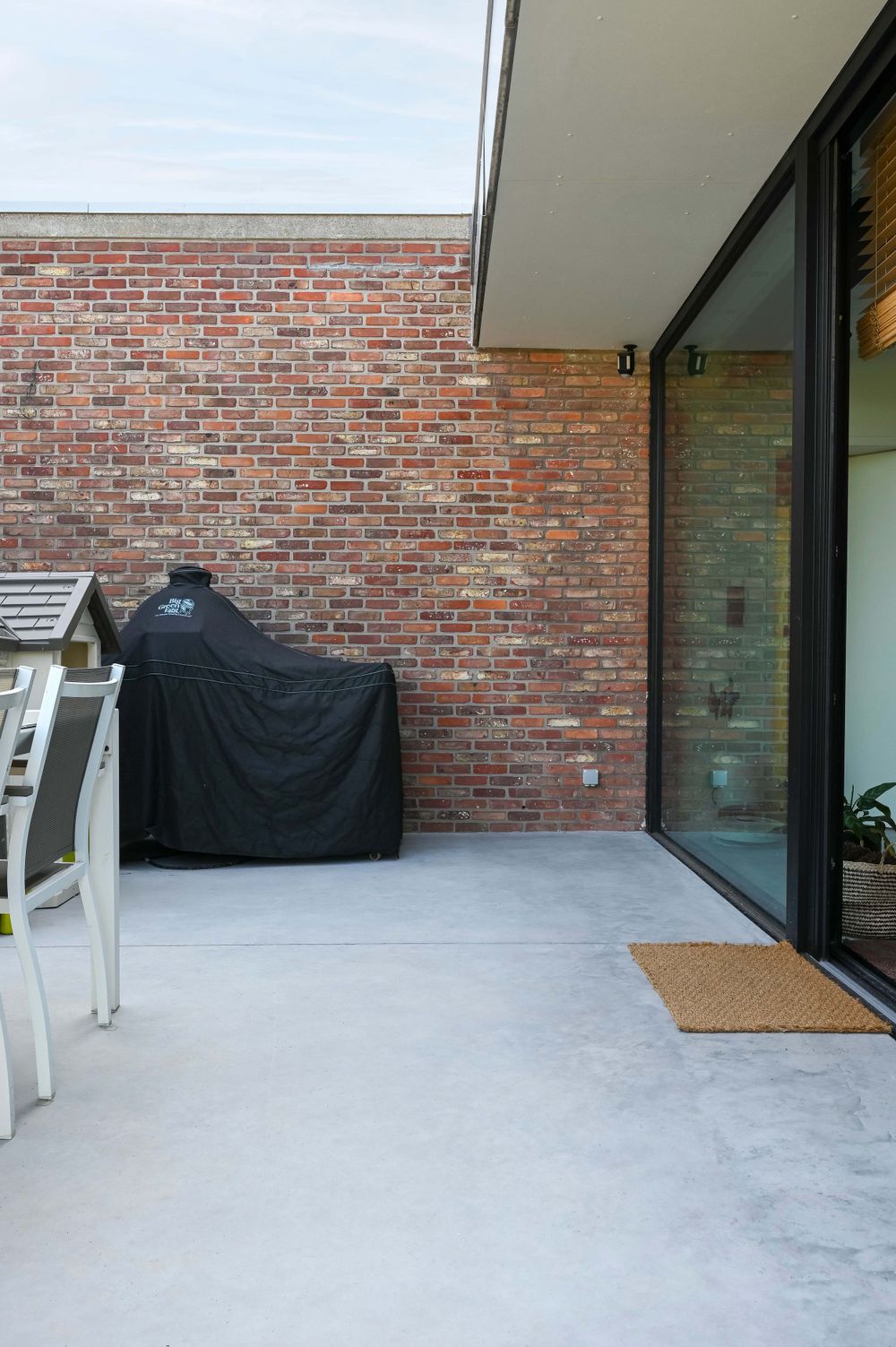 Covered outdoor patio area with concrete flooring and exposed brick wall.