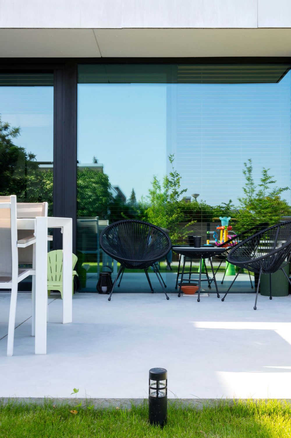Modern outdoor patio space with black acapulco chairs and white tables against glass windows.