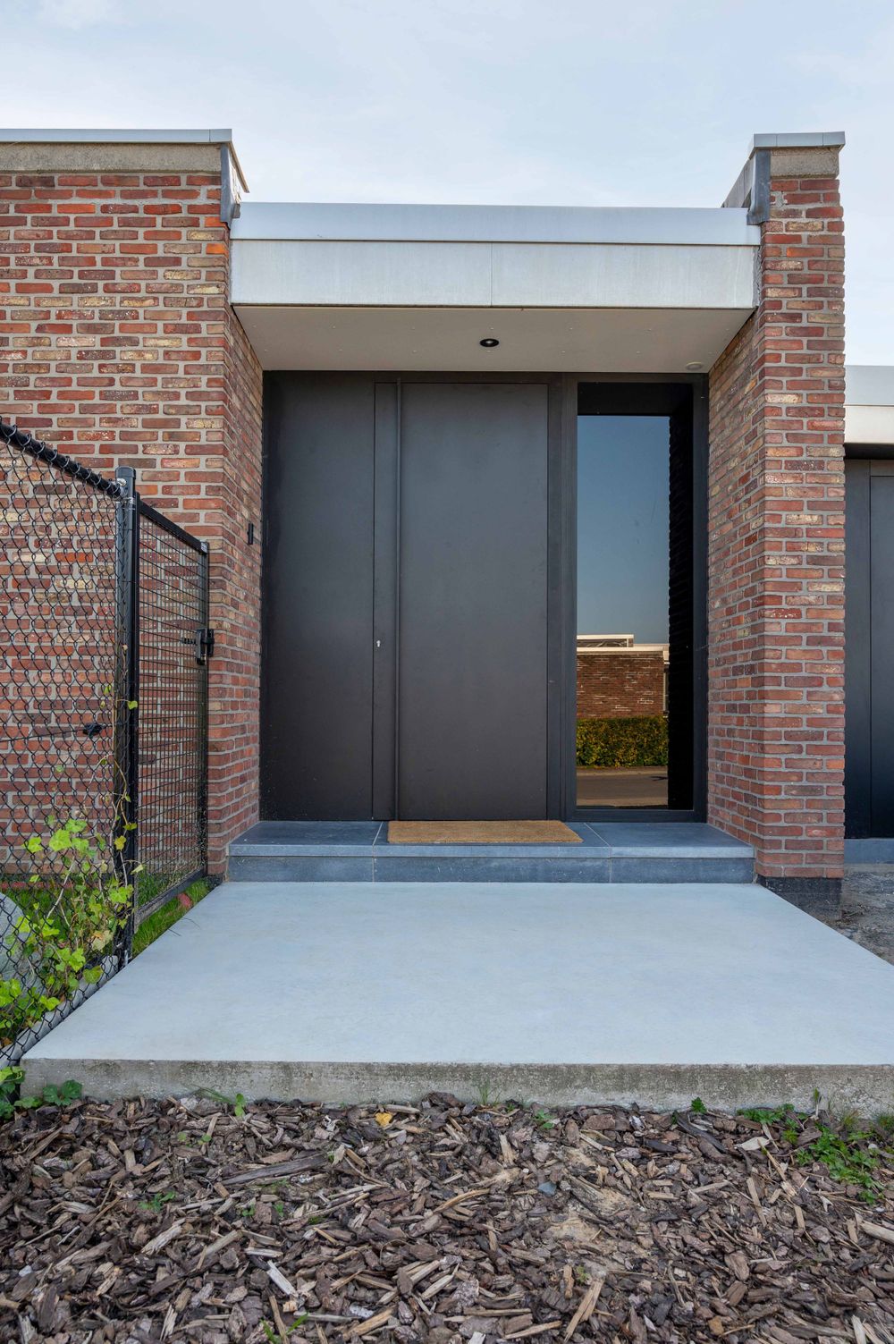 Modern brick exterior entrance with dark gray doors and concrete landing pad.