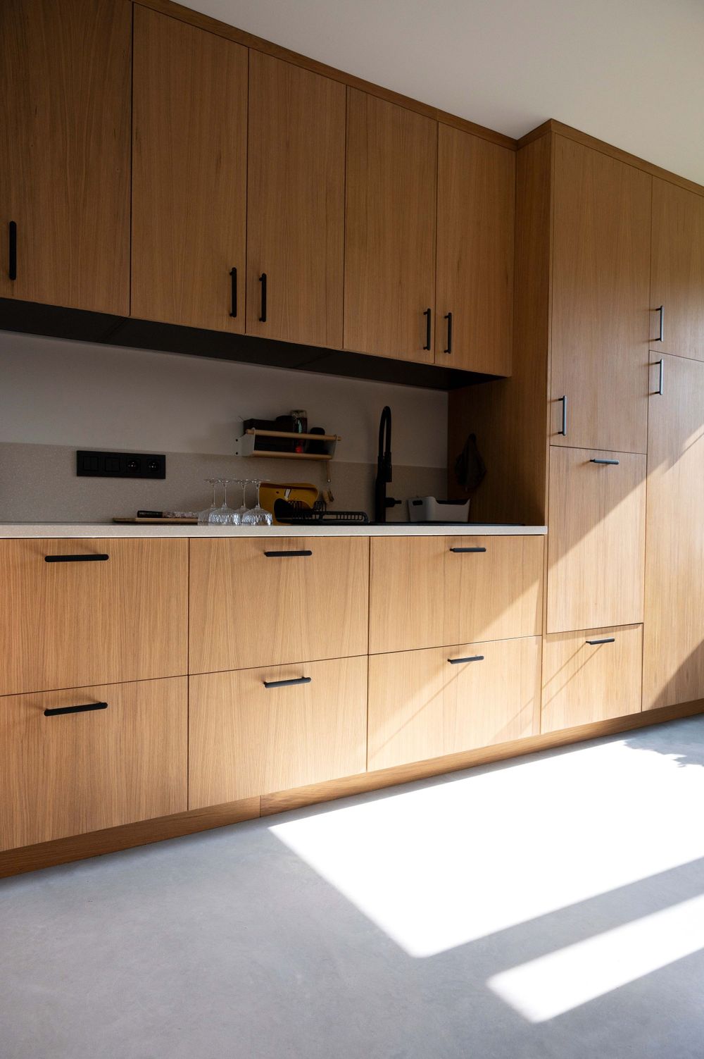 Built-in wooden storage cabinets with black handles illuminated by natural sunlight.