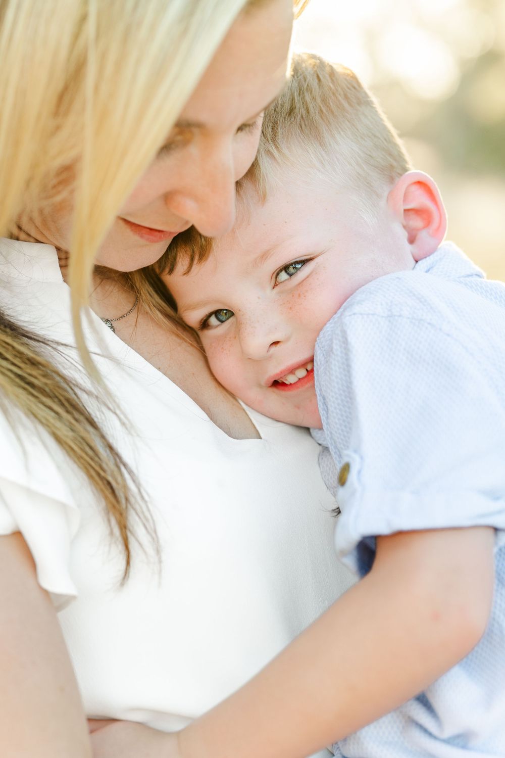 A mother embracing her young son closely, their faces pressed together in an intimate and loving moment.