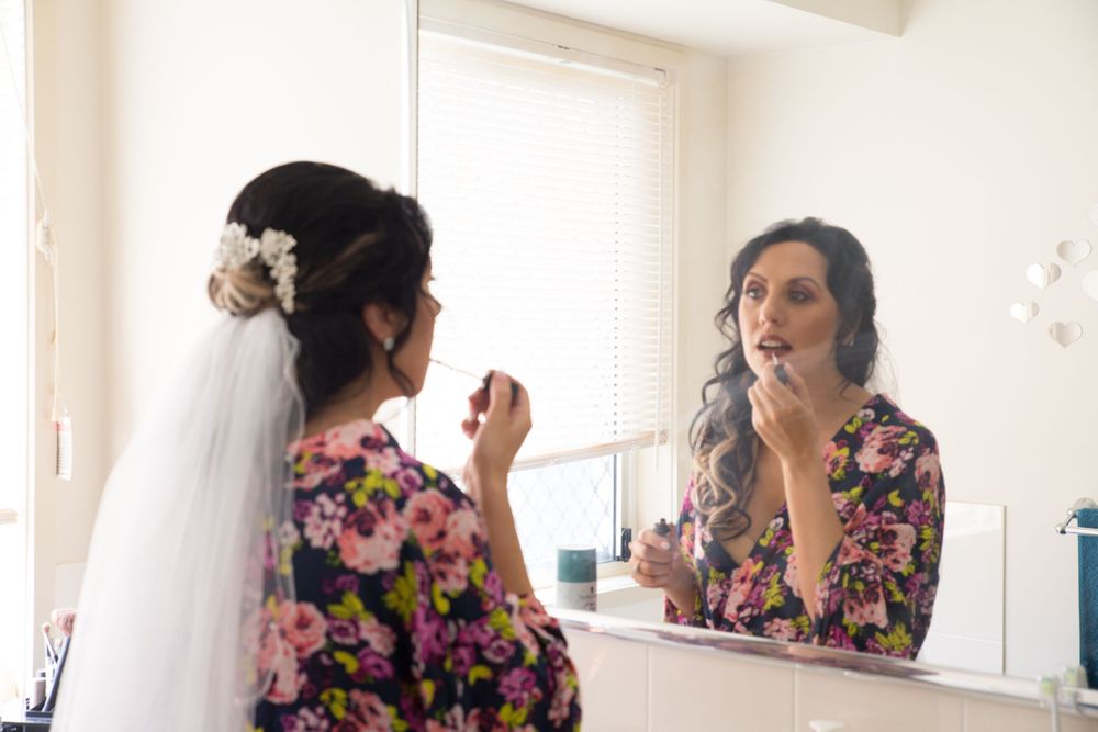 Woman wearing floral pattern dress adjusting her hair in front of mirror.