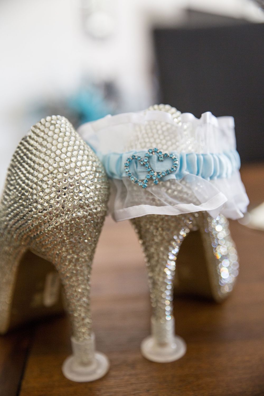 Elegant bridal shoes with rhinestone details and blue garter on wooden surface.